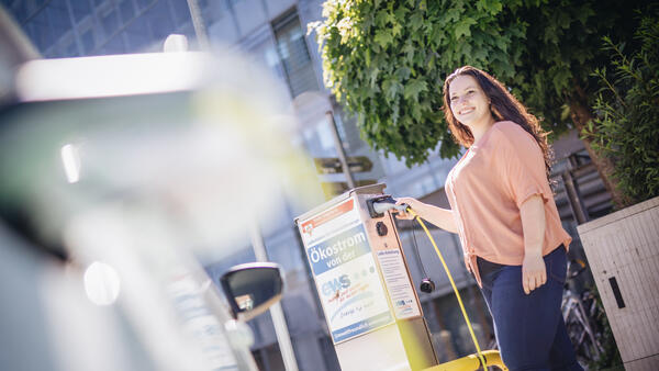 Eine junge Frau betankt ein Elektroauto vor dem Hauptgebäude des Kreises an einer Ladestation.