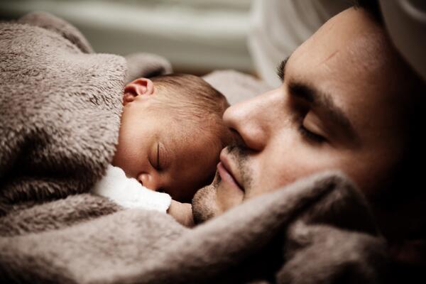 Ein Vater liegt mit einem Neugeborenen im Bett und schläft.