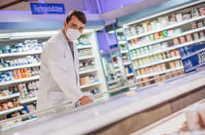 Kreismitarbeiter im weißen Kittel und mit Mundschutz bei einer Lebensmittelkontrolle im Supermarkt.