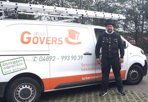 Schornsteinfeger Jelle Johannes Govers steht vor seinem Dienstwagen in typisch schwarzer Kleidung.