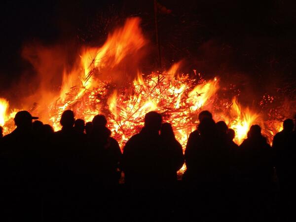Menschen stehen abends vor einem großen Feuer.