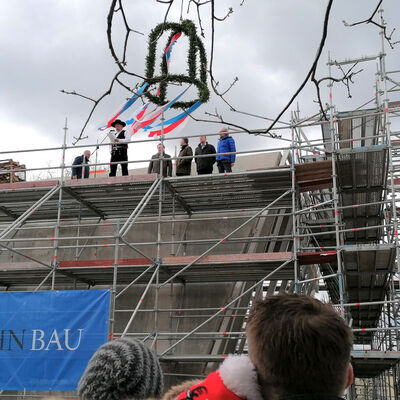 Zu sehen ist eine Außensicht auf den Rohbau des BBZ Bad Segeberg. Über dem Gebäude hängt eine Richtkrone.