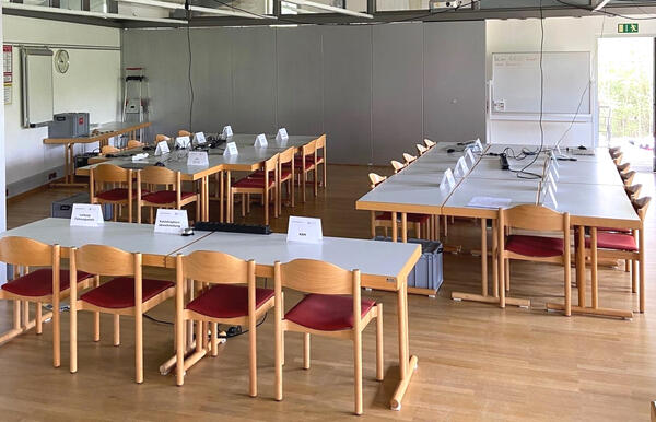 In einem großen Raum stehen mehrere Tische und Stühle in verschiedenen Gruppen zusammen. Auf den Tischen stehen Kärtchen mit den jeweiligen Sachgebieten des Katastrophenschutzes.