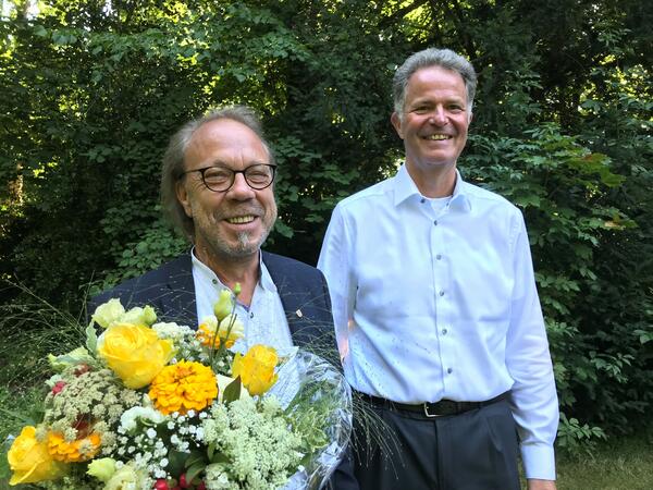 Thorsten Luckow und Landrat Schröder. Im Hintergrund sind Bäume. Herr Luckow hält einen Blumenstrauß in der Hand.