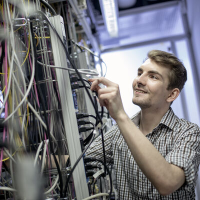 Ein Kreis-Mitarbeiter kontrolliert die Kabel am Server und lächelt.