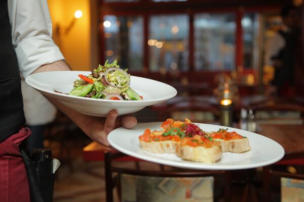 Ein Kellner serviert zwei Teller mit Salat und Bruschetta in einem Restaurant.