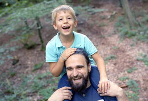 In einem Wald sitzt ein Junge auf den Schultern eines Mannes.
