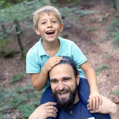 In einem Wald sitzt ein Junge auf den Schultern eines Mannes.