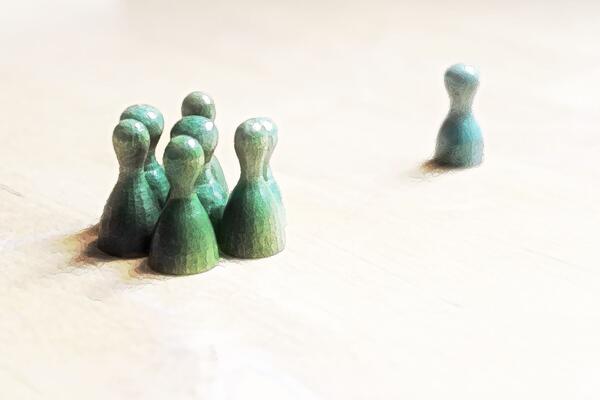 Grüne Spielfiguren stehen zusammen in einer Grupe. Eine einzelne blaue Spielfigur steht in einiger Entfernung daneben.