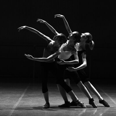 Ein Schwarzweiß-Foto von drei Ballerinas, die versetzt hintereinander stehen und somit den Eindruck einer Bewegung entstehen lassen.
