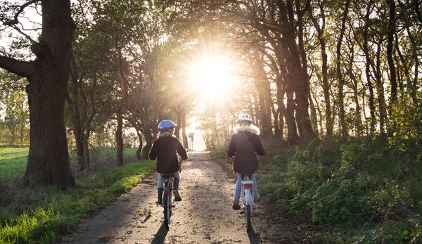 Zwei Mädchen fahren mit dem Fahrrad auf einem Waldweg.