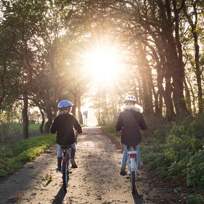 Zwei Mädchen fahren mit dem Fahrrad auf einem Waldweg.