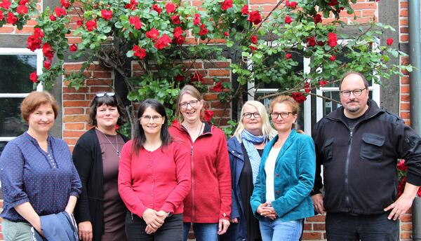 Das Foto zeigt das Team des Erwachsenen-Sozialdienstes (von links): Isabel Juritz, Dörte Meyer, Ilka Schumacher, Katja Lohmeier, Kerstin Schwarzloh, Carmen Wischeropp und Holger Lange. Sie stehen vor einer von Rosen bewachsenen Hauswand. Es fehlen Annina Budnick und Susanne Gehrt.