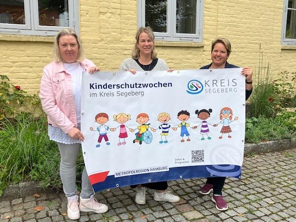 Drei Frauen stehen vor dem Haus Segeberg und halten ein Plakat in den Hnden.