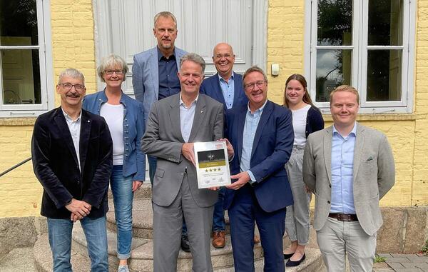 Mehrere Personen stehen zu einem Gruppenfoto versammelt vor dem Haus Segeberg. In der Mitte stehen der Landrat und Matthias Olten (Jobware). Gemeinsam halten sie ein Zertifikat.