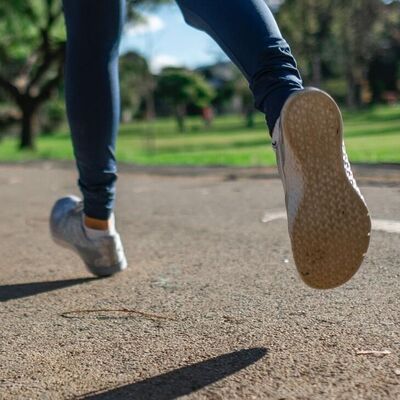 Auf dem Bild sieht man zwei Beine, die mit Joggingschuhen &uuml;ber Asphalt laufen. Im Hintergrund ist ein Park mir B&auml;umen und Wiese.
