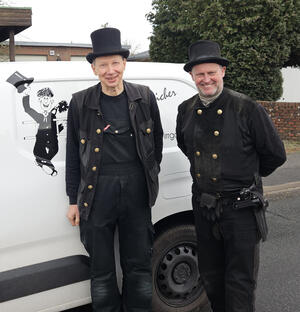 Zwei Männer in schwarzer Schornsteinfegerbekleidung lachen in die Kamera.