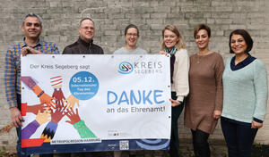 Zwei Mnner und vier Frauen stehen vor einer Wand und halten lachend ein Banner mit der Aufschrift "Danke an das Ehrenamt!" hoch.