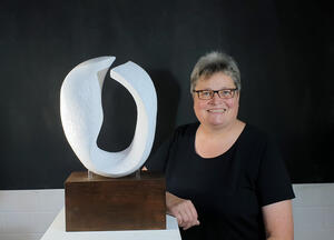 Anne Germelmann steht neben einem Podest mit ihrer weißen Skulptur. Die Skulptur erinnert ein wenig an ein "O" oder ein Ohr.