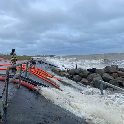 Mehrere Schläuche der Feuerwehr münden in die Ostsee. Das Wasser strömt den Deich hinunter.