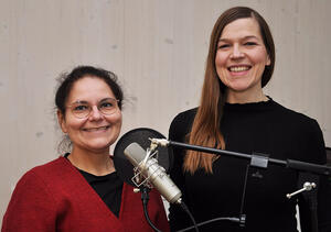 Zwei Frauen stehen vor einem Mikrofon und lächeln.