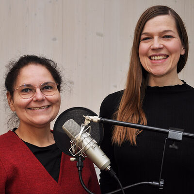 Zwei Frauen stehen vor einem Mikrofon und lächeln.