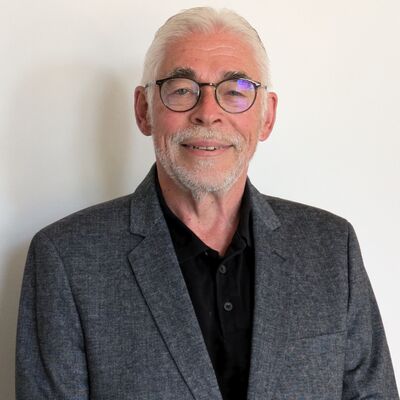 Ein grauhaariger Mann mit Brille. Er trägt ein graues Sakko.