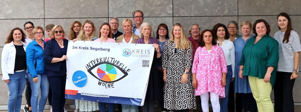 Viele Frauen und Männer stehen mit einem Plakat für die IKW vor einer grauen Wand.