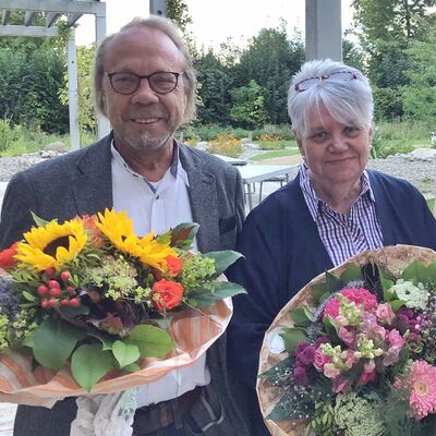 Zwei Menschen mit Blumensträußen in der Hand.