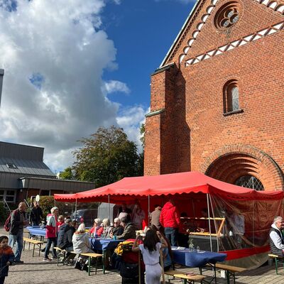 Ein Stand mit roter Plane und vielen Menschen vor einer Kirche.