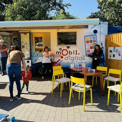 Mehrere Menschen sitzen oder stehen vor einem weißen geöffneten LKW, der begehbar ist.