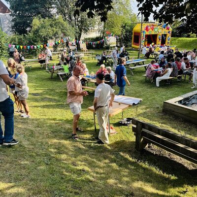 Viele Menschen sitzen und stehen auf einer grünen Wiese und unterhalten sich.