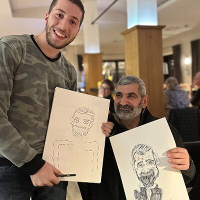 Zwei Männer halten jeweils eine gezeichnete Karikatur von sich selbst in den Händen.