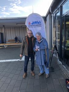 Ein Mann und eine Frau stehen vor einer Art Ladenfenster und einem Aufstellbanner des Behindertenbeirates.