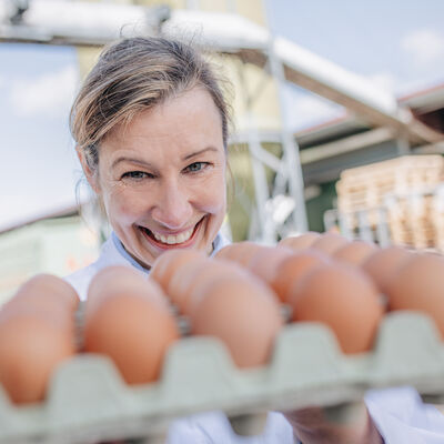 Eine Mitarbeiterin des Kreises kontrolliert eine Palette Eier und lächelt.