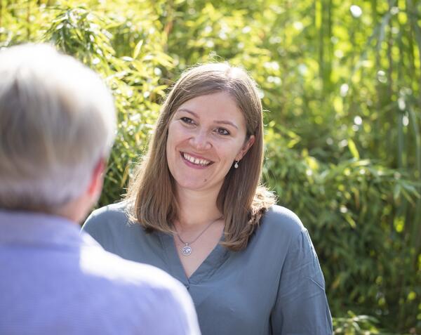 Eine junge Frau spricht mit einer Seniorin im Garten und lächelt.