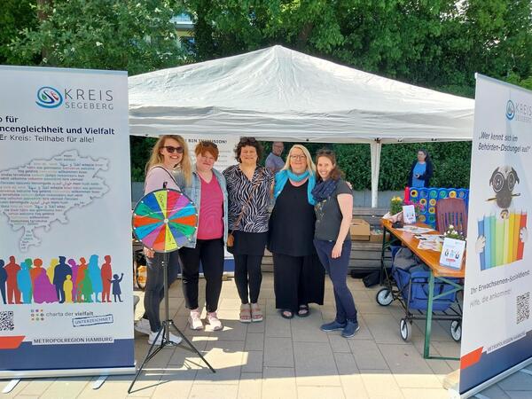 Mehrere Frauen stehen vor einem weißen Pavillon und neben vielen bunten Aufstellern mit Informationen.