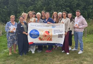 Frauen und Männer stehen in einem grünen Garten und halten ein Plakat hoch.