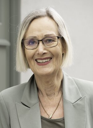 Eine Frau trägt ein graues Sakko und lächelt. Das Bild zeigt ihr Portrait.