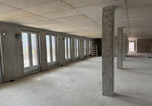 Eine Innenaufnahme des Erdgeschosses im Neubau "Haus A". Der Rohbau ist noch ohne einzelne Räume, sondern besteht nur aus einem Flur aus grauem Beton.