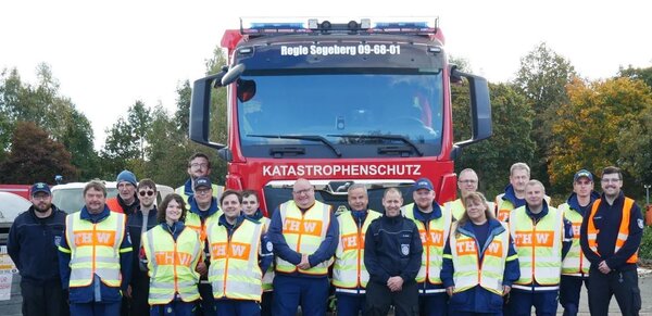 Einsatzkräfte stehen vor einem Fahrzeug des Katastrophenschutzes des Kreises Segeberg.