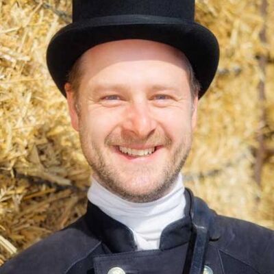 Ein Schornsteinfeger mit schwarzem Hut steht vor einem Heuhaufen.