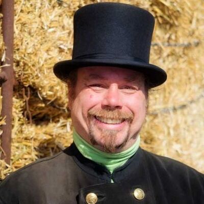 Ein Schornsteinfeger mit schwarzem Hut steht vor einem Heuhaufen.