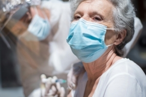 Eine Seniorin mit blauem Mundschutz wird von einer anderen Frau geimpft.