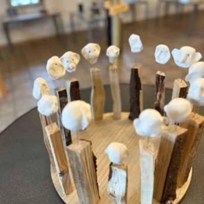 Auf einem Tisch steht ein runder Holzboden mit Holzst&auml;bchen in einem Kreis. Auf den H&ouml;lzern sind wei&szlig;e Menschenk&ouml;pfe aufgespie&szlig;t.