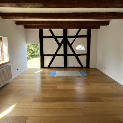 In einem Sportraum mit Holzfu&szlig;boden und Holzbalken liegt eine Yoga-Matte in der Mitte.