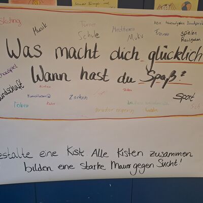 Ein Plakat mit aufgeschrieben W&ouml;rtern. In der Mitte steht der Satz: "Was macht dich gl&uuml;cklich?"