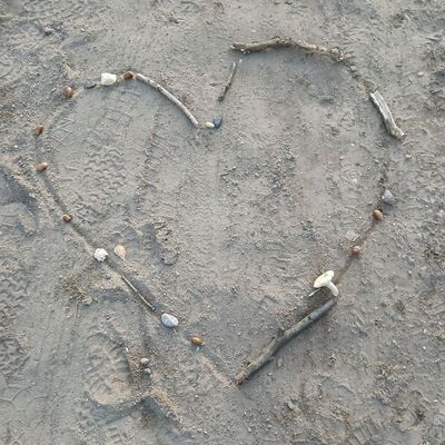 Aus Stein und St&ouml;ckern wurde ein Herz auf Sand gebildet.