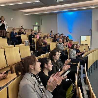 Menschen sitzen in einem H&ouml;rsaal und klatschen.