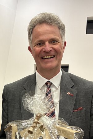 Ein Mann mittleren Alters mit Jacket und Krawatte lacht in die Kamera.